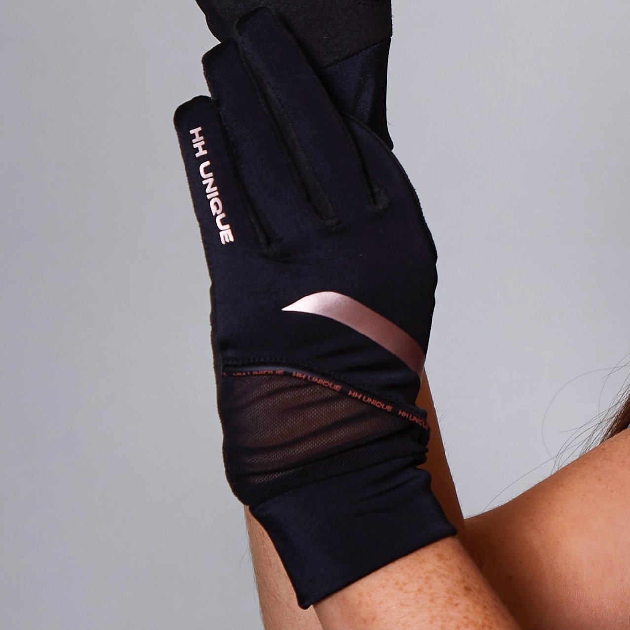 Black and Rose Gold riding gloves.  Photo shows left hand, HH unique logo runs down little finger and a rose gold strip diagonally across the top of the hand.  Mesh towards the wrist with a comfortable cuff around the wrist.